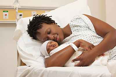 Woman hugging her newborn baby while laying down on hospital bed.